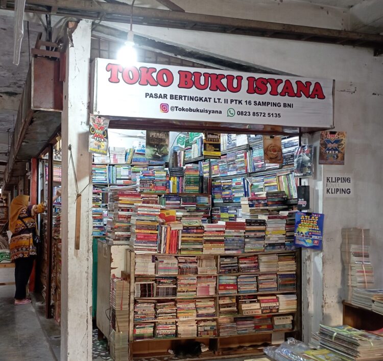 Penjual toko buku bekas, Vivi sedang merapikan buku-buku bekas tokonya di gedung oranye lantai dua Pasar Raya Padang, Minggu (2/4/2023) (Aisyah Luthfi/Genta Andalas)